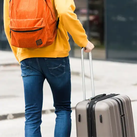 Male with orange backpack walking with suitcase